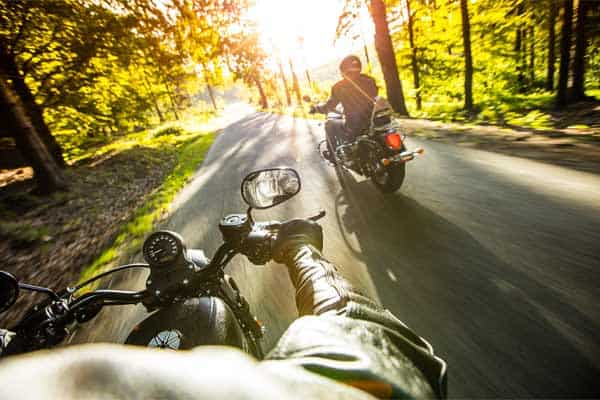 Two motorcycle riders on a road in a wooded area.